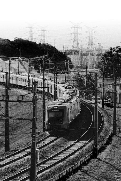 Black and white of train going through railway station with posts in daytime