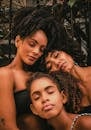 Multi generational African American ladies and girl with closed eyes and curly hair leaning head on each other in daytime in street