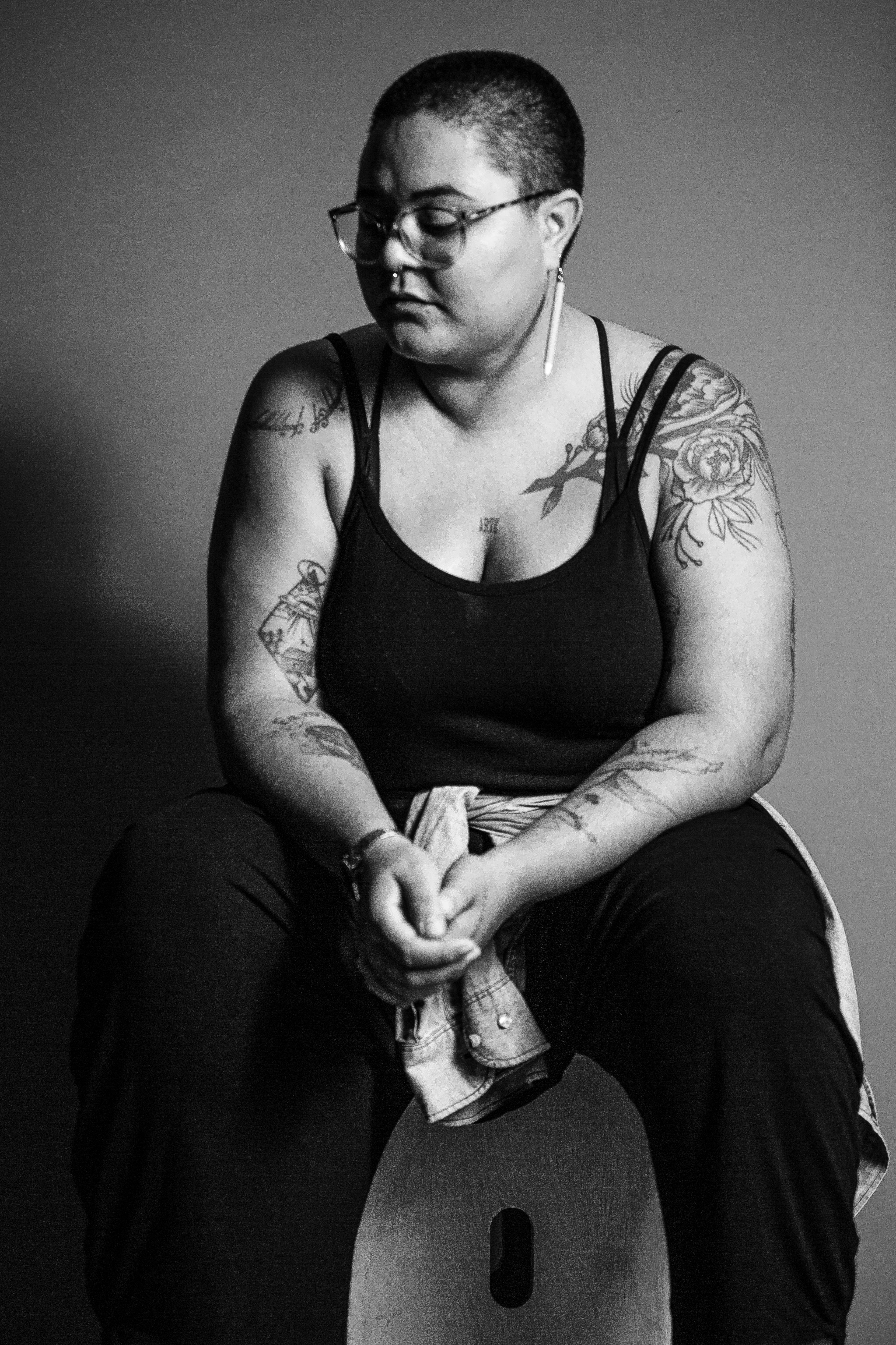 Artistic black and white portrait of a tattooed woman sitting indoors.