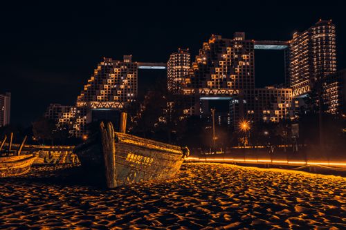 Free Captivating view of Qinhuangdao's skyline at night with illuminated buildings and wooden boats on the sand. Stock Photo