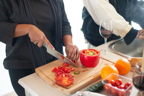 Free A person slices bell peppers on a cutting board while cooking, alongside fresh produce in a kitchen setting. Stock Photo