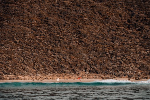 Serene beach scene with rugged cliffs, gentle waves, and distant people enjoying the shore.