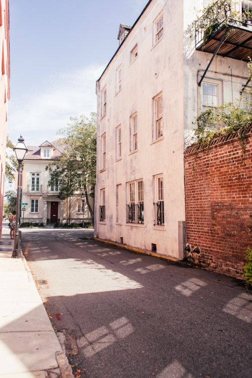 Free A quaint narrow street lined with old buildings and a brick wall under a clear blue sky. Stock Photo