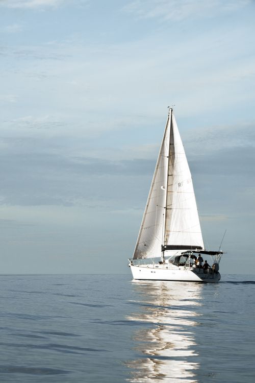 Free White sailboat gliding on tranquil sea under a bright sky, capturing nautical serenity. Stock Photo