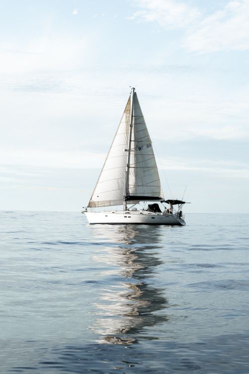 Free Sailboat gliding peacefully on calm sea with clear sky reflections. Stock Photo