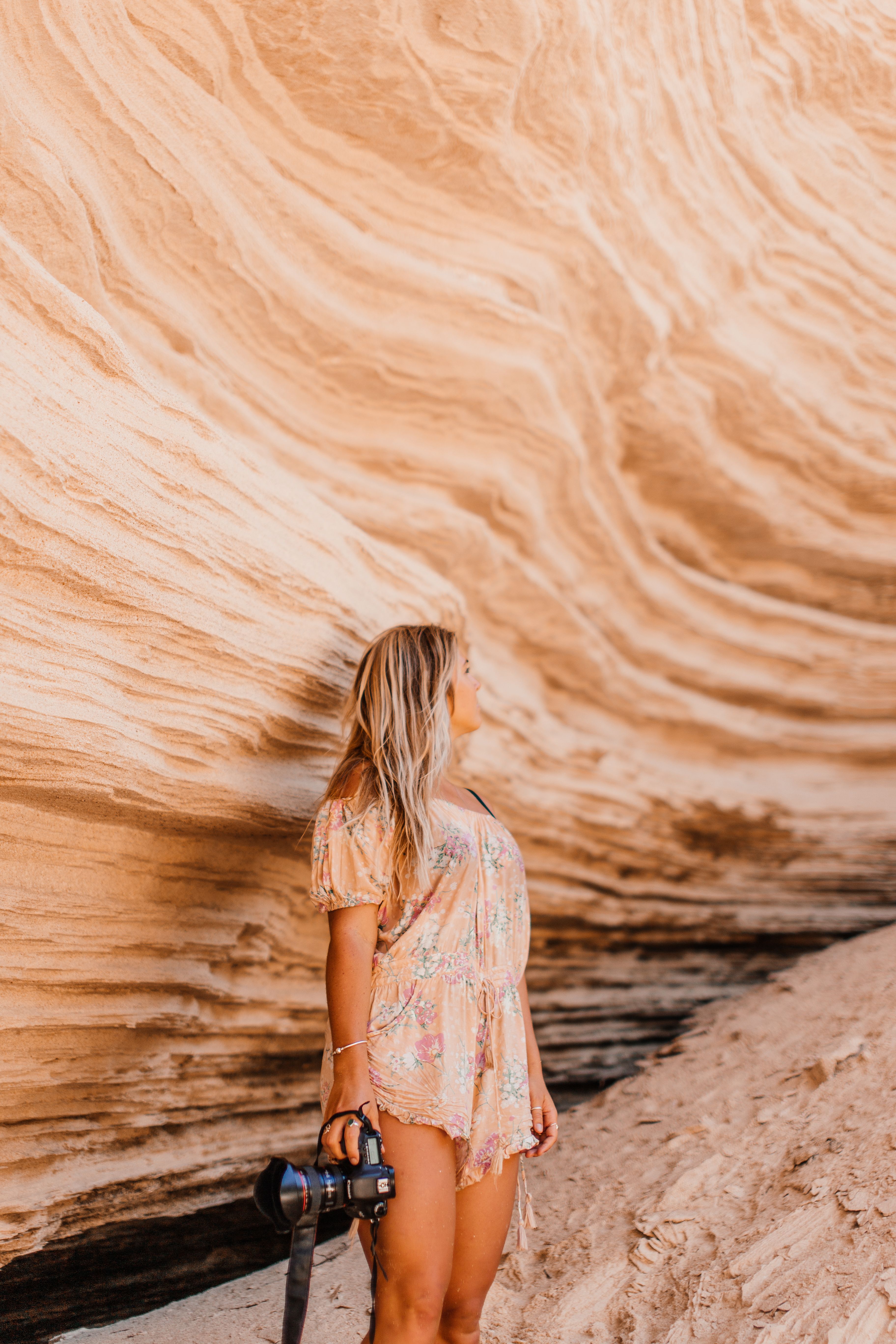 A woman holding a camera stands near a striking sandstone rock formation, embodying adventure and exploration.
