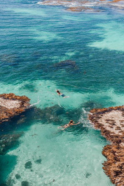 Aerial photo of people swimming in transparent turquoise waters surrounded by rocky formations.