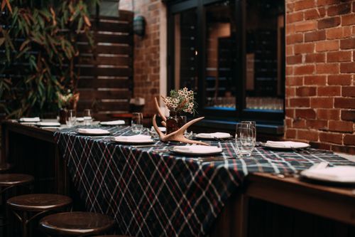Free Elegant table setting with plaid tablecloth and flowers in a rustic brick-walled room, ideal for dining concepts. Stock Photo