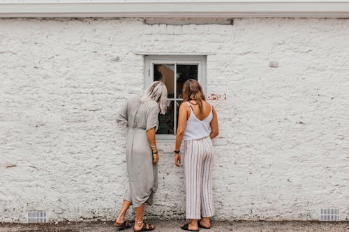 Free Women Looking inside a House Through a Window Stock Photo