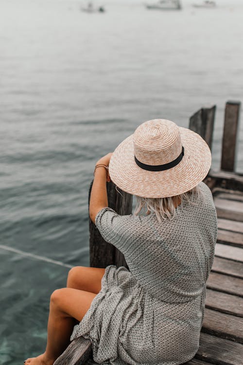 Woman in Sun Hat and Gray Dress Sitting on a Wooden Dock