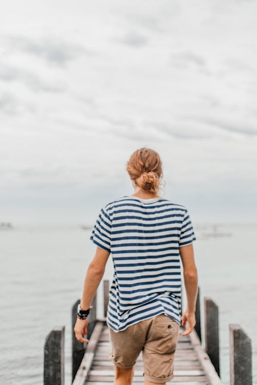 A Person Wearing a Striped Shirt and Shorts Walking on a Wooden Dock