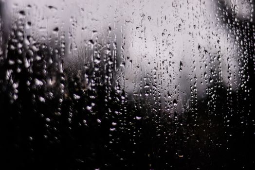 Artistic close-up of raindrops on glass, creating a moody grayscale ambiance.