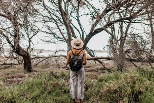 Woman with backpack and straw hat exploring a leafless forest in summer.