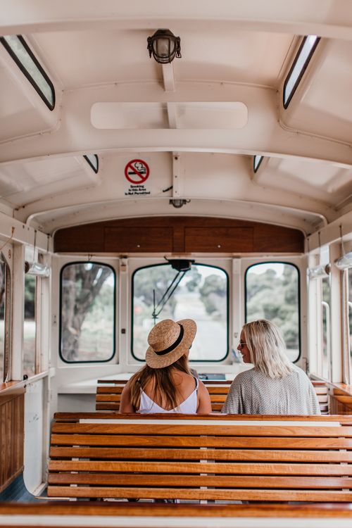 Free Two women sitting on a wooden bench in a tram, enjoying a leisurely day. Stock Photo