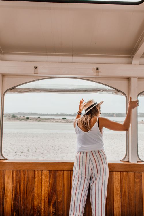 Free Young woman in summer attire standing by a boat window, gazing outdoors. Stock Photo