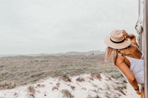 Free A woman in a straw hat leans from a vehicle to enjoy a vast desert view, capturing a sense of summer adventure. Stock Photo