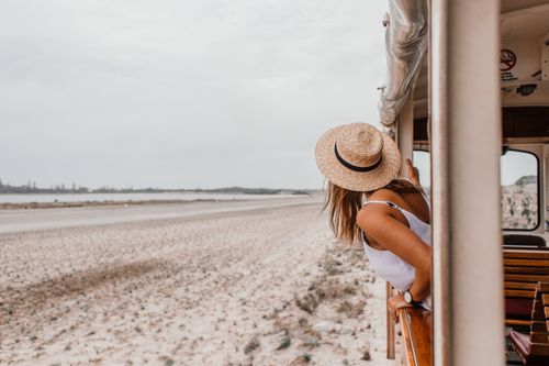 Free Woman in straw hat leans out of a train window, enjoying a beachside journey. Stock Photo