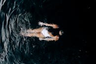 迷人的俯视图，一名女子在黑暗的水中游泳，周围是涟漪