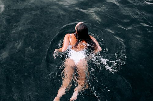 Free Aerial view of a woman swimming in clear sea water, creating splashes and ripples. Stock Photo