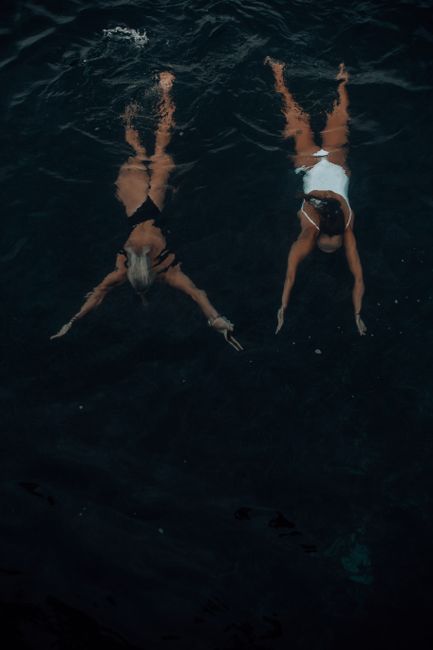 Overhead shot of two women swimming in deep, dark water, showcasing a serene vacation moment.