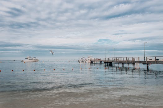 A peaceful seascape featuring yachts docked near a wooden pier under a cloudy sky.