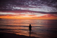 一名女子在充满活力的日落和色彩缤纷的天空中走在海滩上的宁静轮廓