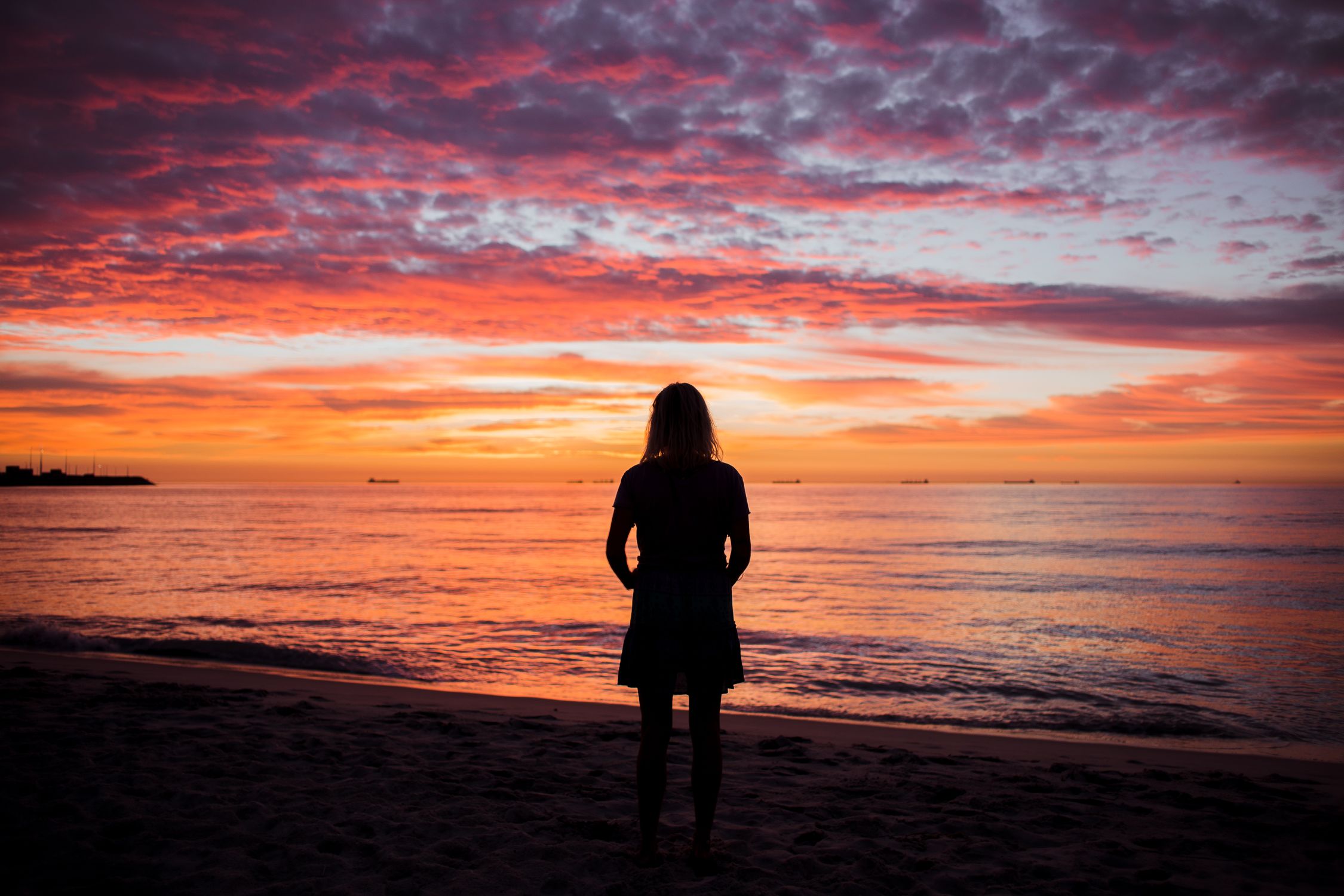 Silhouette of a Woman Standing on a Beach at Sunset · Free Stock Photo