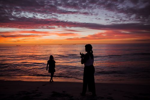 Free Silhouette of two people on sandy beach during a tranquil sunset with colorful sky and calm sea. Stock Photo