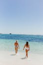 两个女人在泳装走在阳光明媚的海滩，享受清澈的蓝色大海和天空.