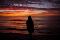 一个女人站在一个生动的橙色和粉红色的日落在海滩上的剪影，捕捉一个宁静的时刻