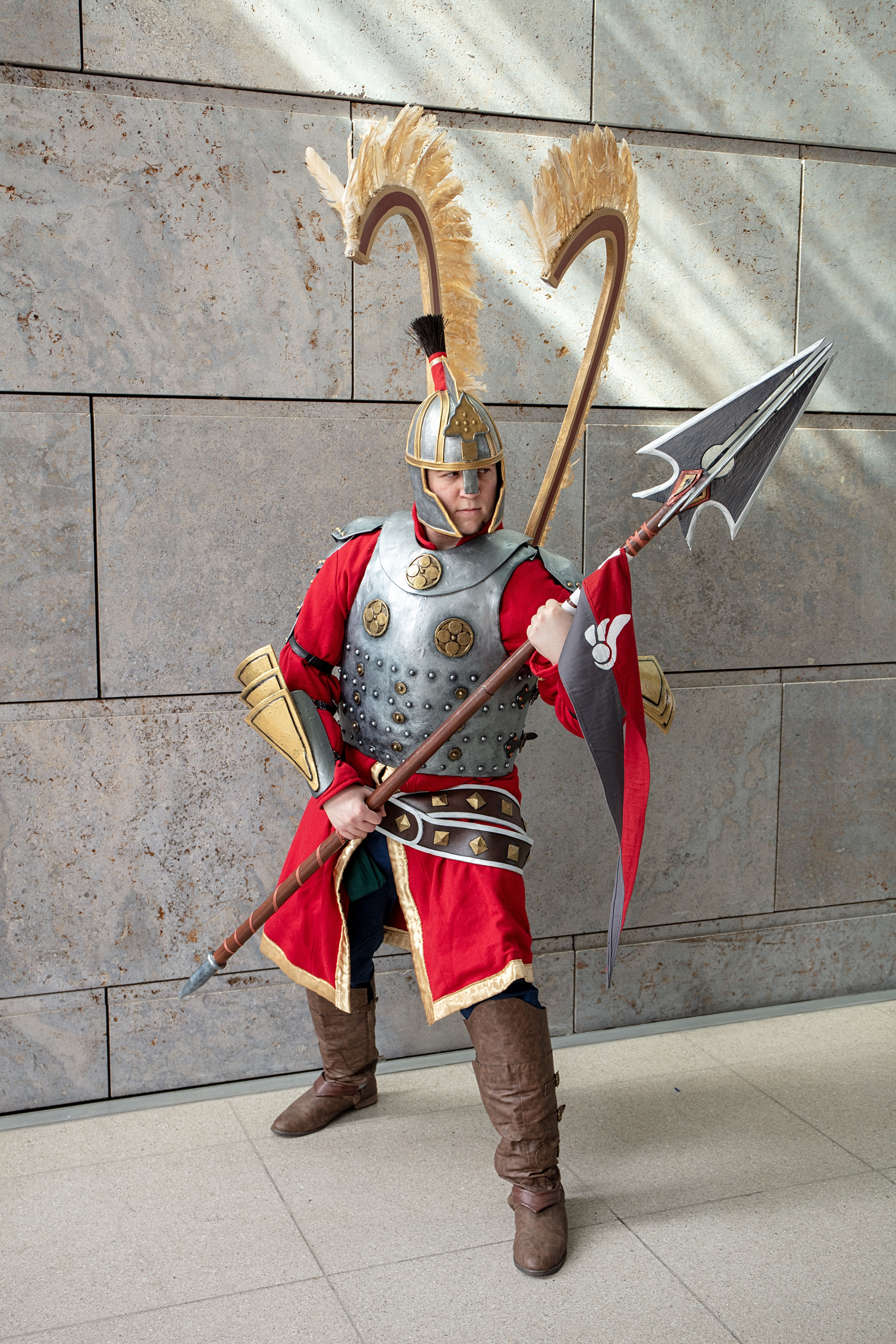A medieval warrior in detailed armor poses with a halberd in indoors setting.