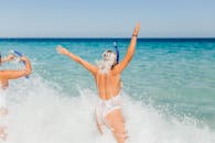 在阳光明媚的日子里，两名穿着泳衣的女子拿着浮潜装备在海浪中溅水