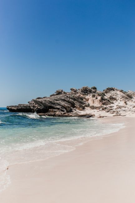 Stunning coastal view featuring sandy beach, rock formations, and clear blue sky.