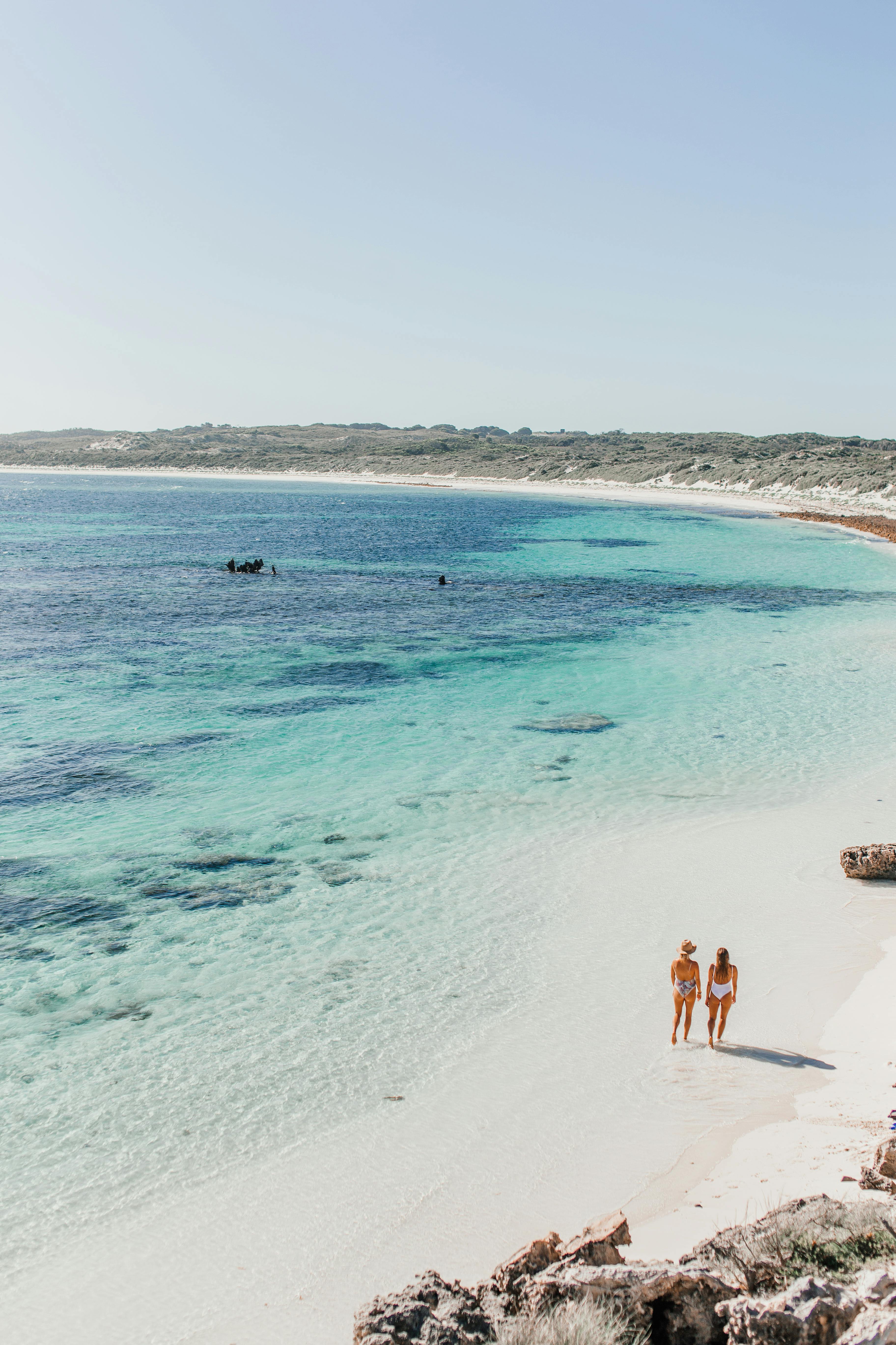 Two women walking along a beautiful deserted beach with turquoise waters.