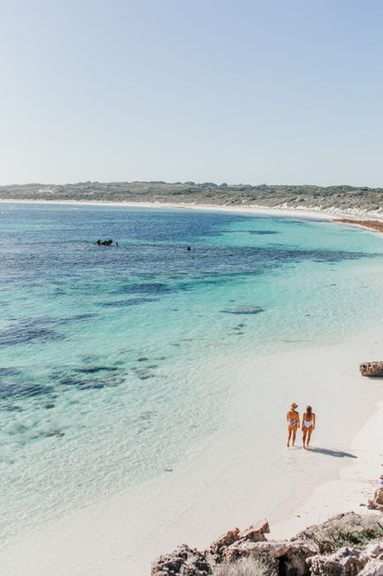 Two women walking along a beautiful deserted beach with turquoise waters.