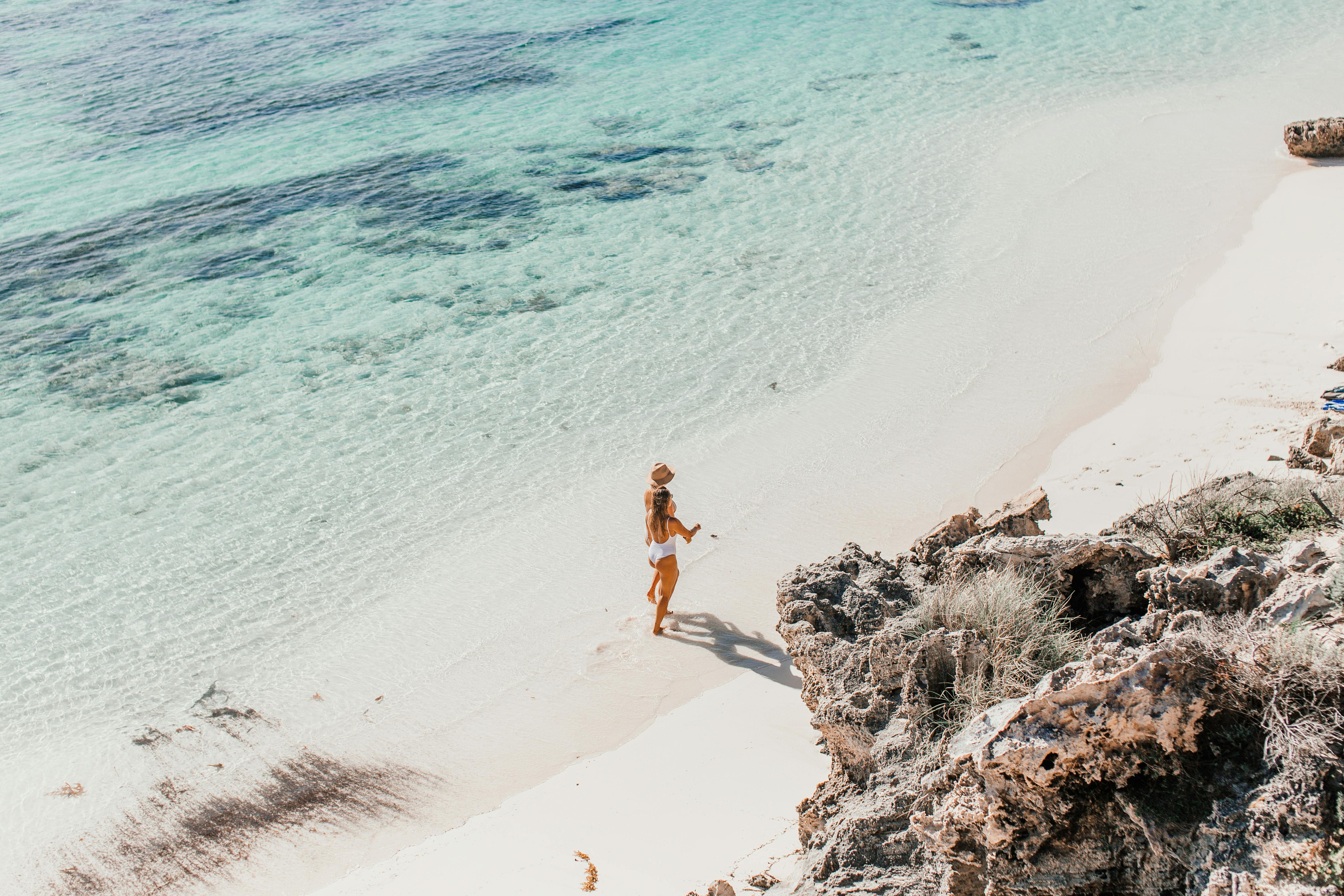 鸟瞰一名妇女沿着阳光明媚、海水清澈的热带海滩行走
