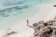 鸟瞰一名妇女沿着阳光明媚、海水清澈的热带海滩行走