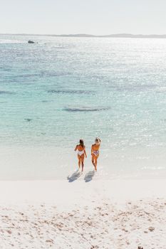 Two women walking on a pristine beach under bright sunlight, embodying relaxation.