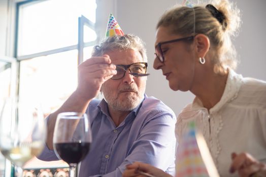 Senior couple celebrating with wine and party hats indoors, conveying joy and companionship.
