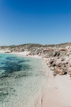 Stunning beach scene with clear water, rocky shoreline, and a bright blue sky.