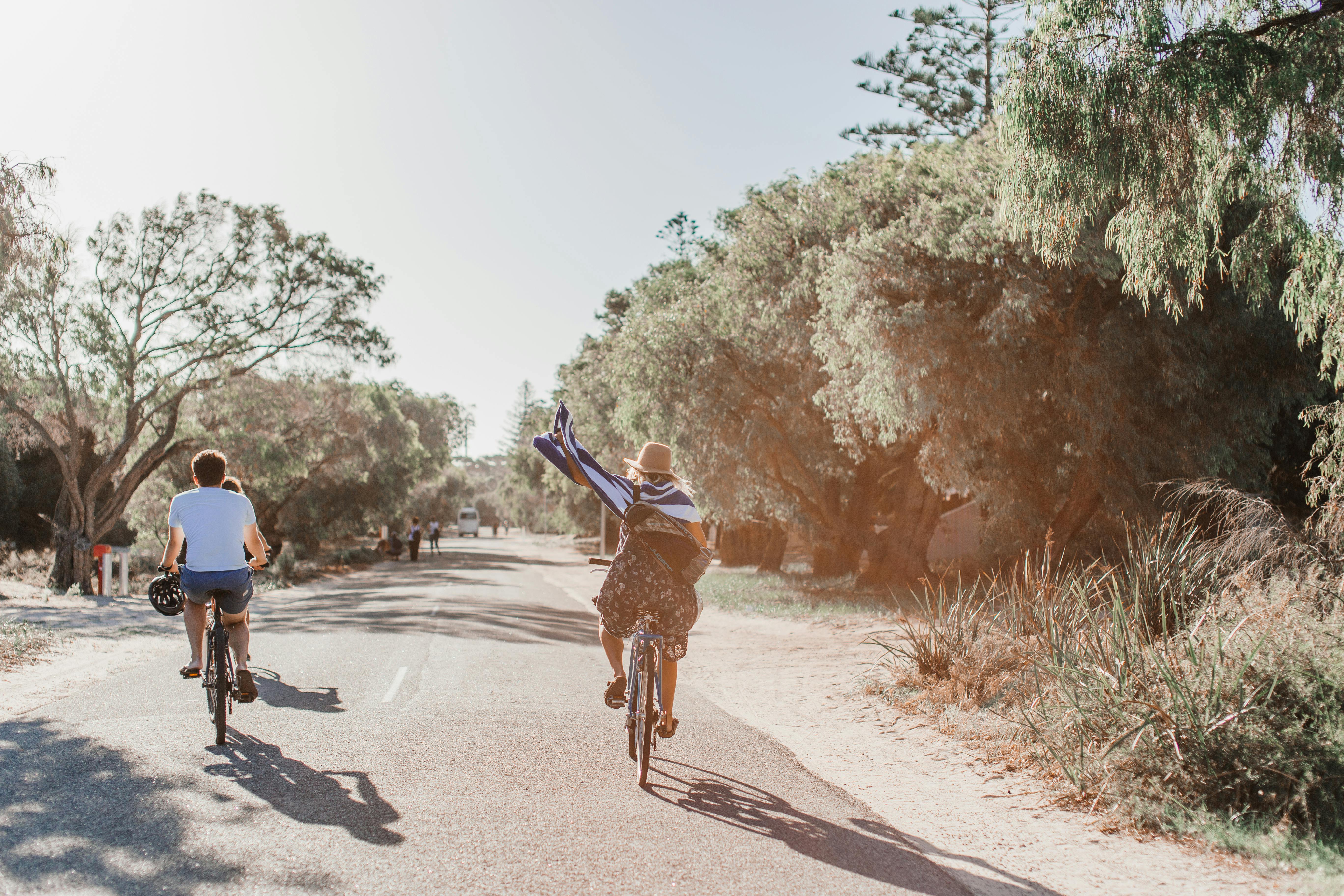 Free Two people cycling on a sunny road surrounded by greenery, enjoying the outdoors. Stock Photo