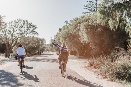 Free Two people cycling on a sunny road surrounded by greenery, enjoying the outdoors. Stock Photo