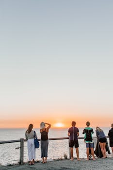 People standing on a seaside boardwalk watching a stunning sunset.