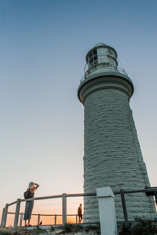 Free A lighthouse with a tourist enjoying a sunset view, framed by a clear blue sky. Stock Photo