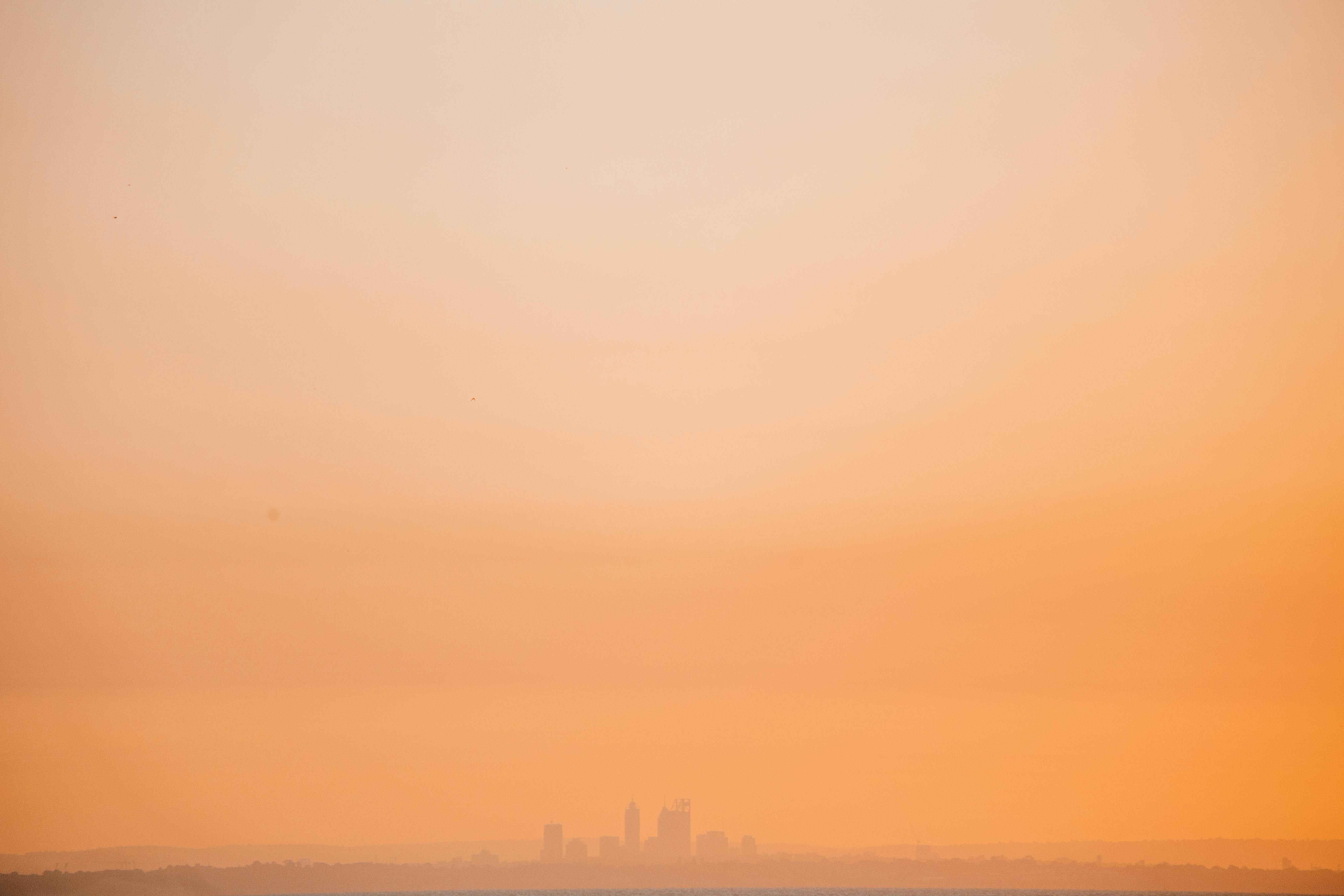 Silhouette of a city skyline shrouded in orange fog during a sunset.