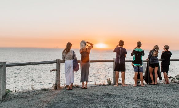 A group of people watching a beautiful sunset over the ocean, their backs to the camera.