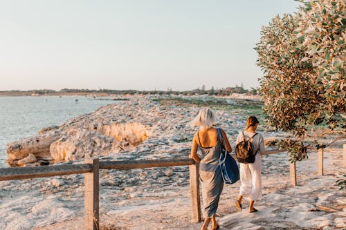 Two Women are Walking Away From Sandy Beach at Sunset