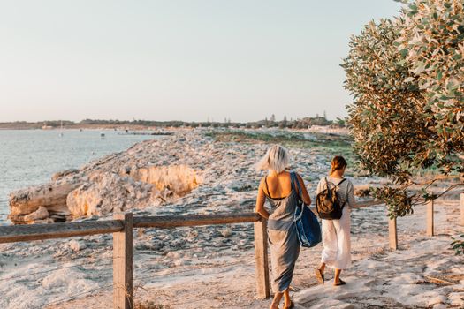 Two Women are Walking Away From Sandy Beach at Sunset