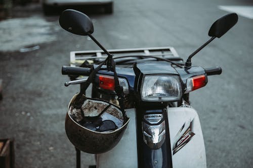 Old fashioned helmet hanging on handlebar of retro metallic motorcycle parked on asphalt road