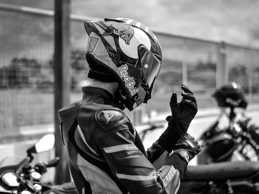 A motorcyclist in racing gear adjusts helmet outdoors with blurred background.